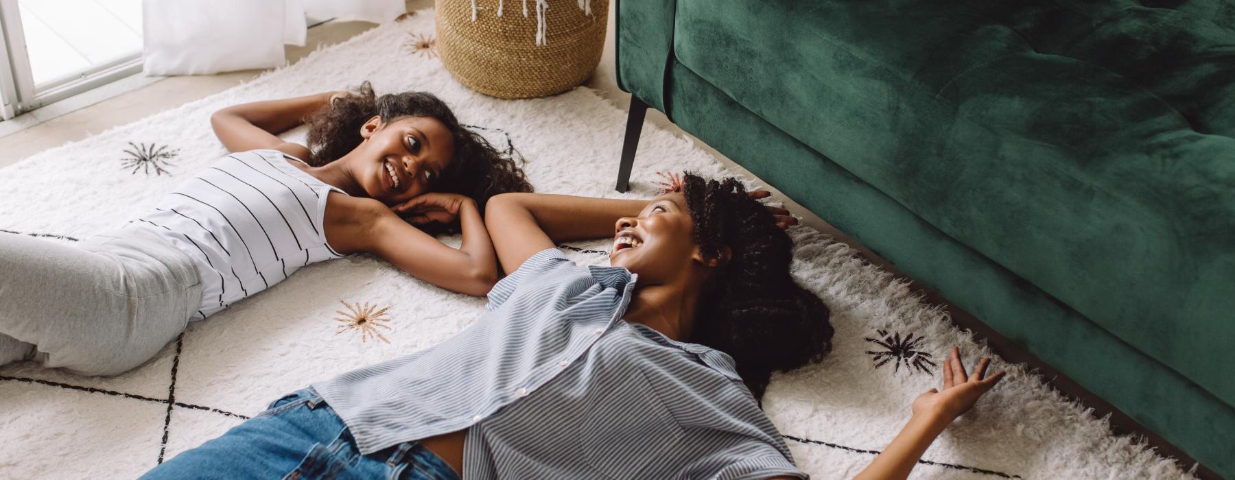 mother and daughter laying on their living room carpet next to couch